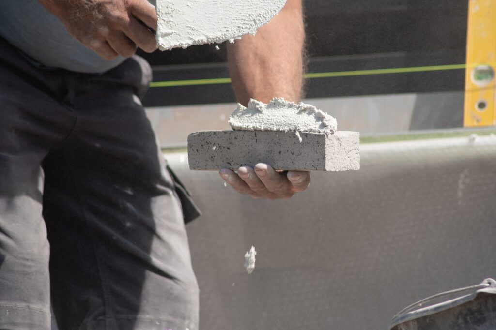 close up of the hands of a bricklayer applying cement mortar to a brick