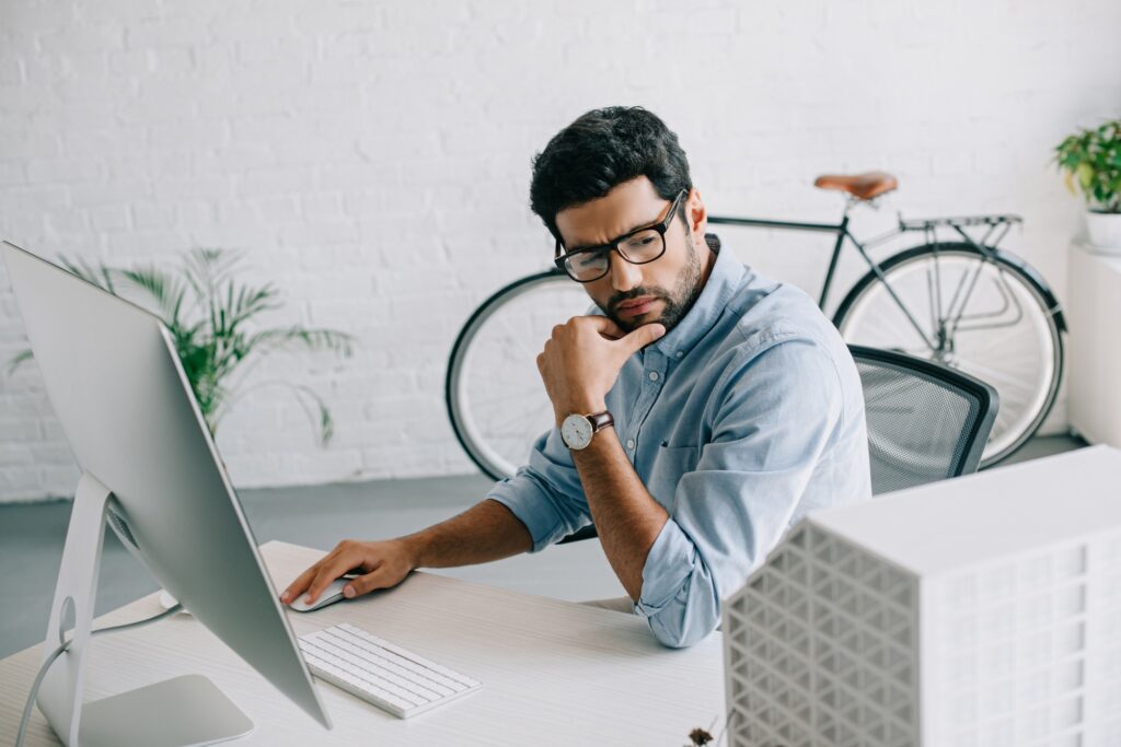 serious handsome architect using computer and looking at architecture model in office